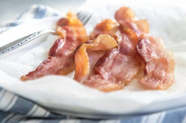 Slices of cooked bacon on paper towels on a white plate.