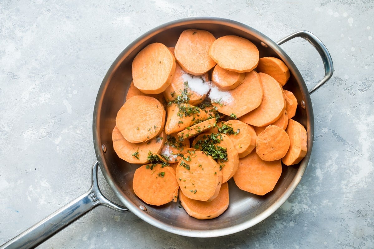 Sliced sweet potatoes and spices in a sliver skillet.