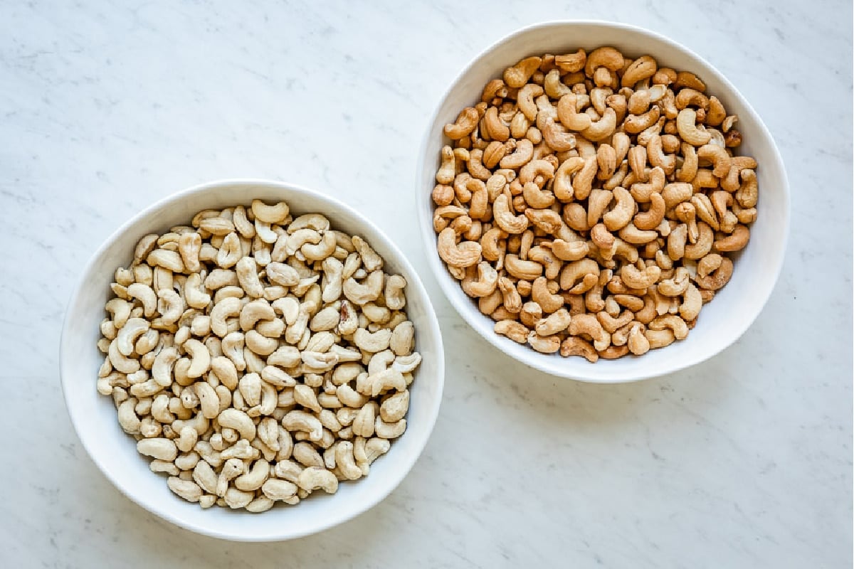 Two bowls of cashews: one raw, one roasted.