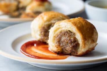 Two sausage rolls on a plate with a swirl of ketchup.