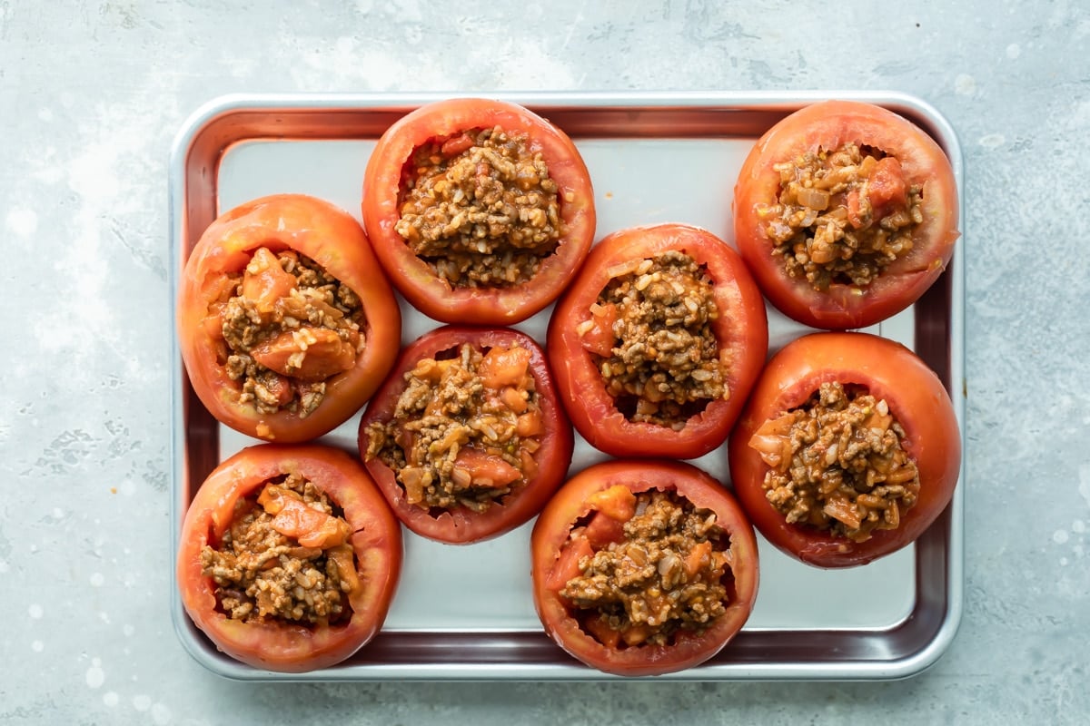 Eight pre-baked taco stuffed tomatoes on a baking pan.
