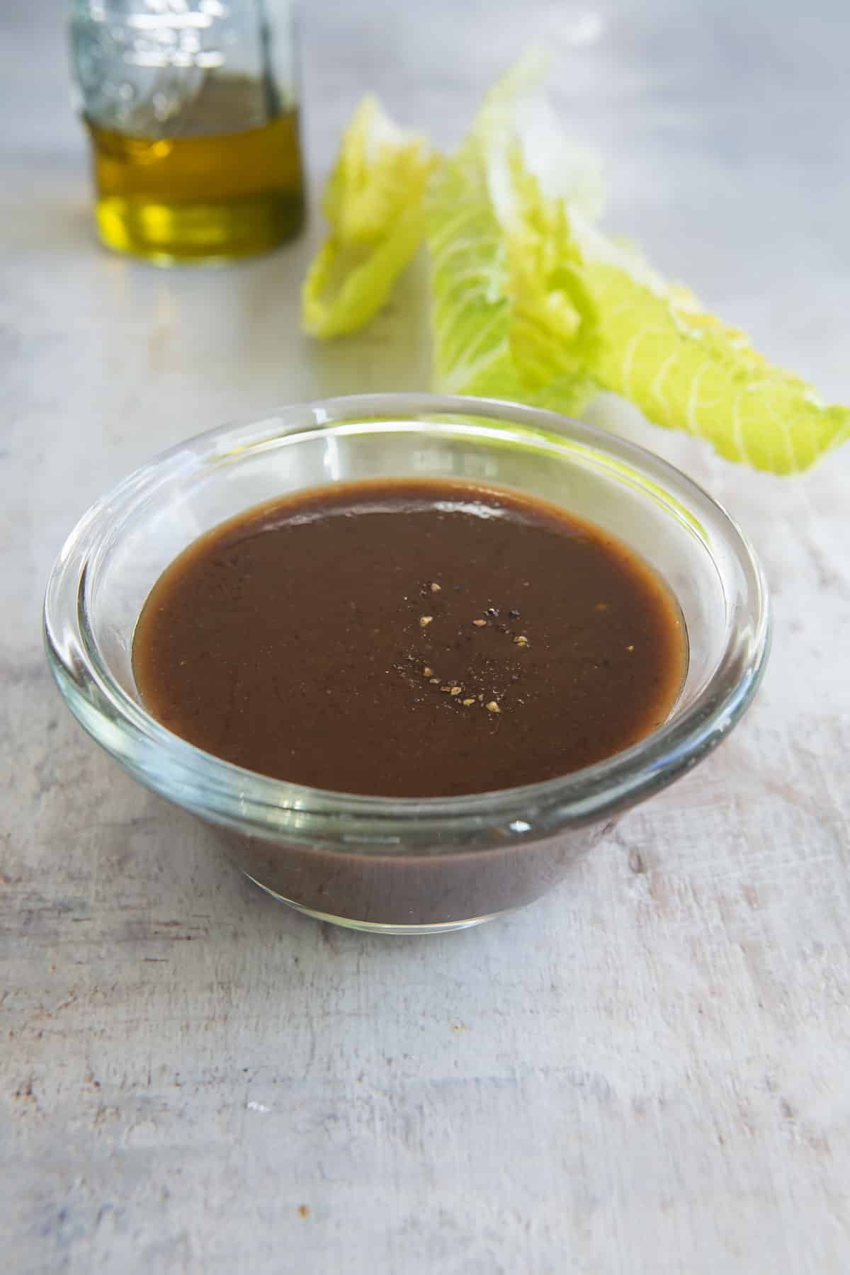 Balsamic Vinaigrette in a clear glass dish next to leafs of romaine lettuce.