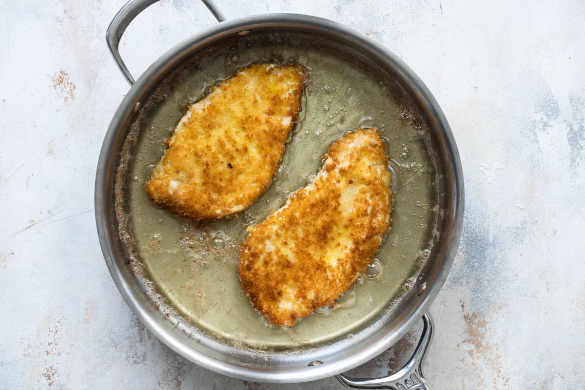 Fried chicken parmesan cutlets in a skillet.