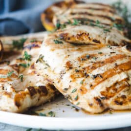 A platter with grilled lemon chicken breasts on it.