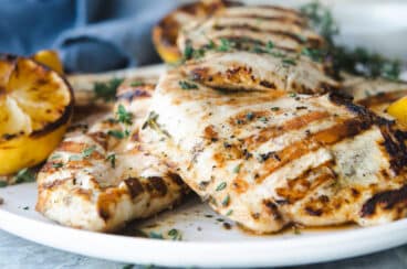A platter with grilled lemon chicken breasts on it.