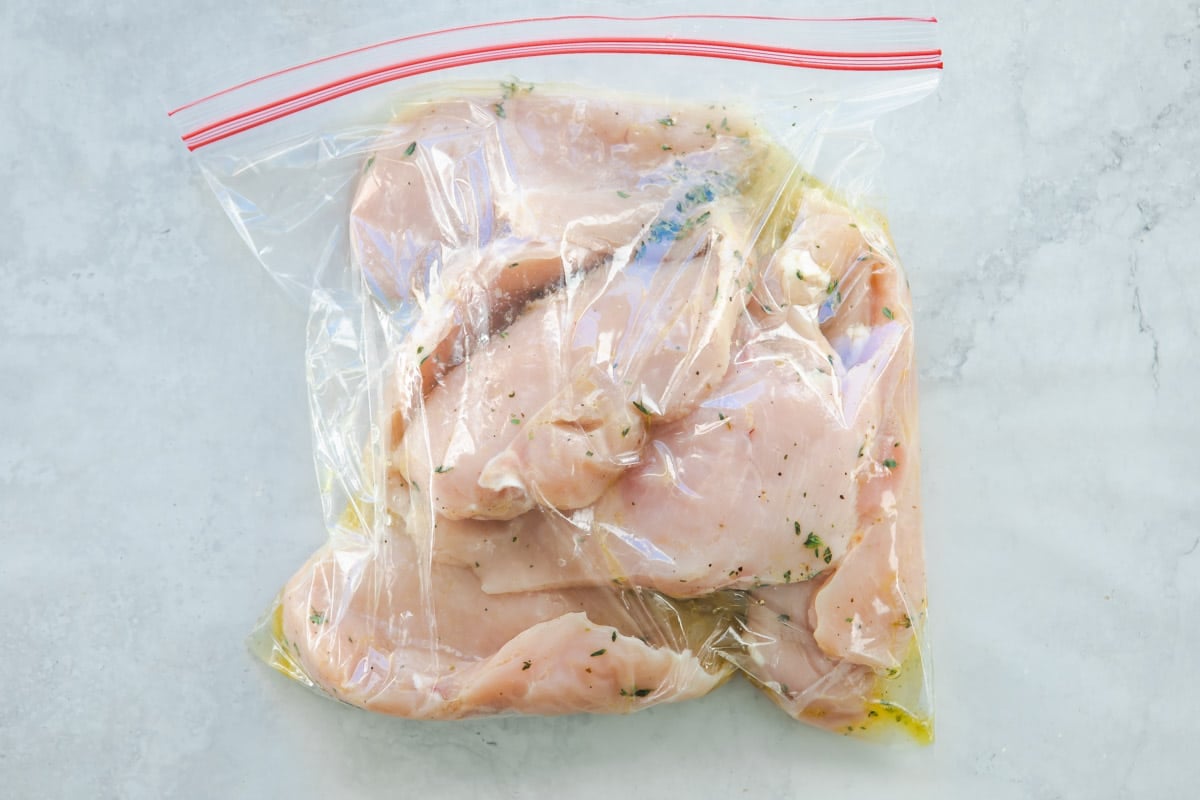 Raw chicken marinating in a plastic bag with lemon juice and thyme.
