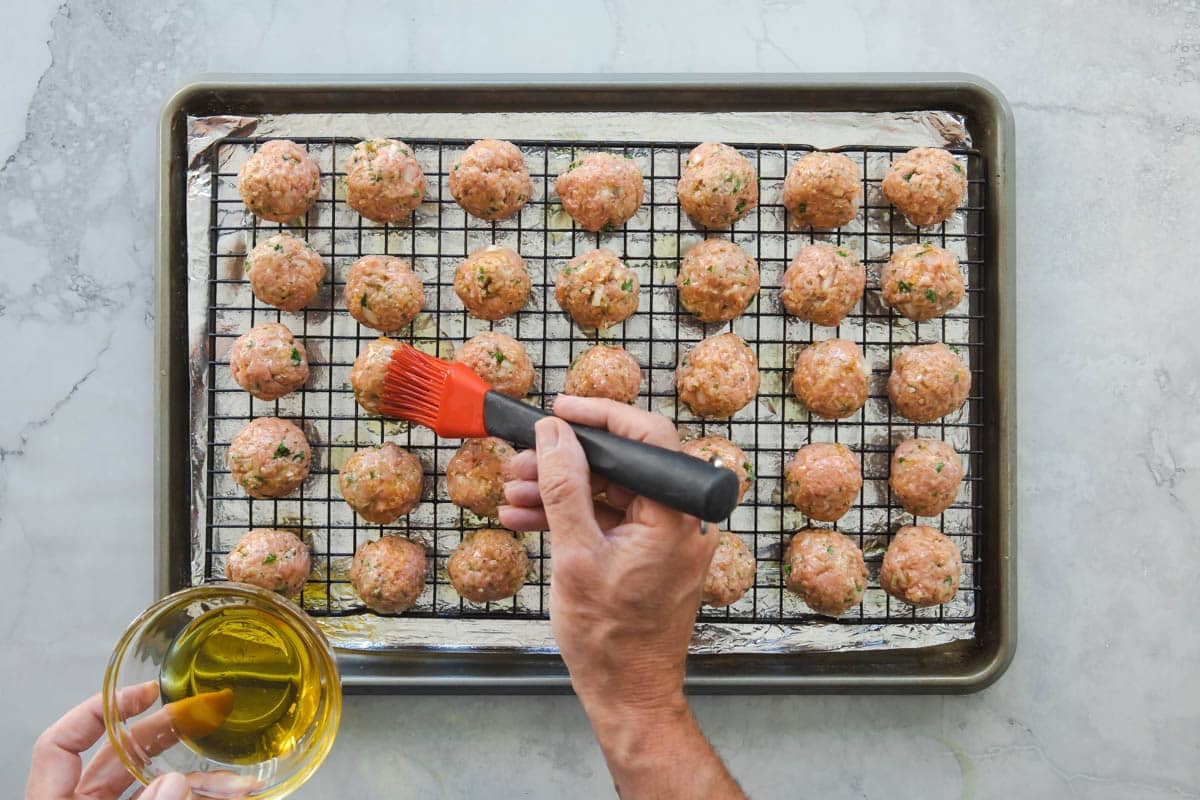 Rows of unbaked meatballs on a baking rack set over a baking sheet.