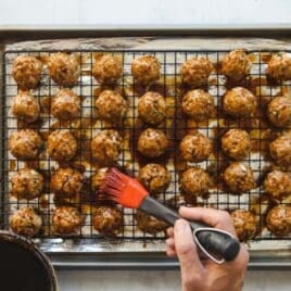 Rows of baked meatballs on a baking rack set over a baking sheet.