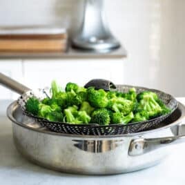 A steam basket full of broccoli in a saucepan.