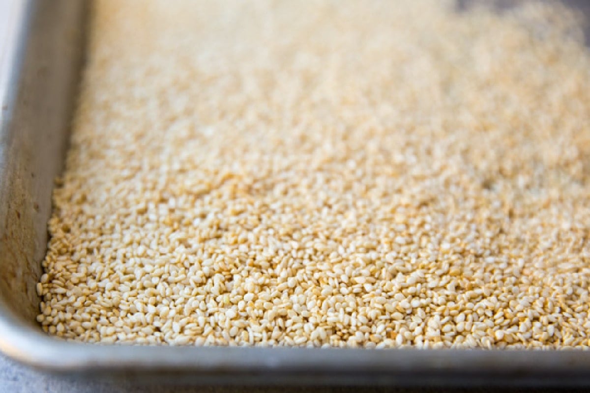 Sesame seeds toasting on a baking sheet.