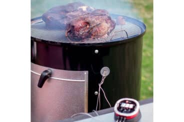 A weber charcoal smoker with meat on top.
