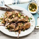 A white platter full of lamb chops garnished with garlic.