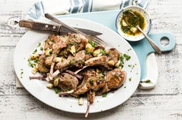 A white platter full of lamb chops garnished with garlic.