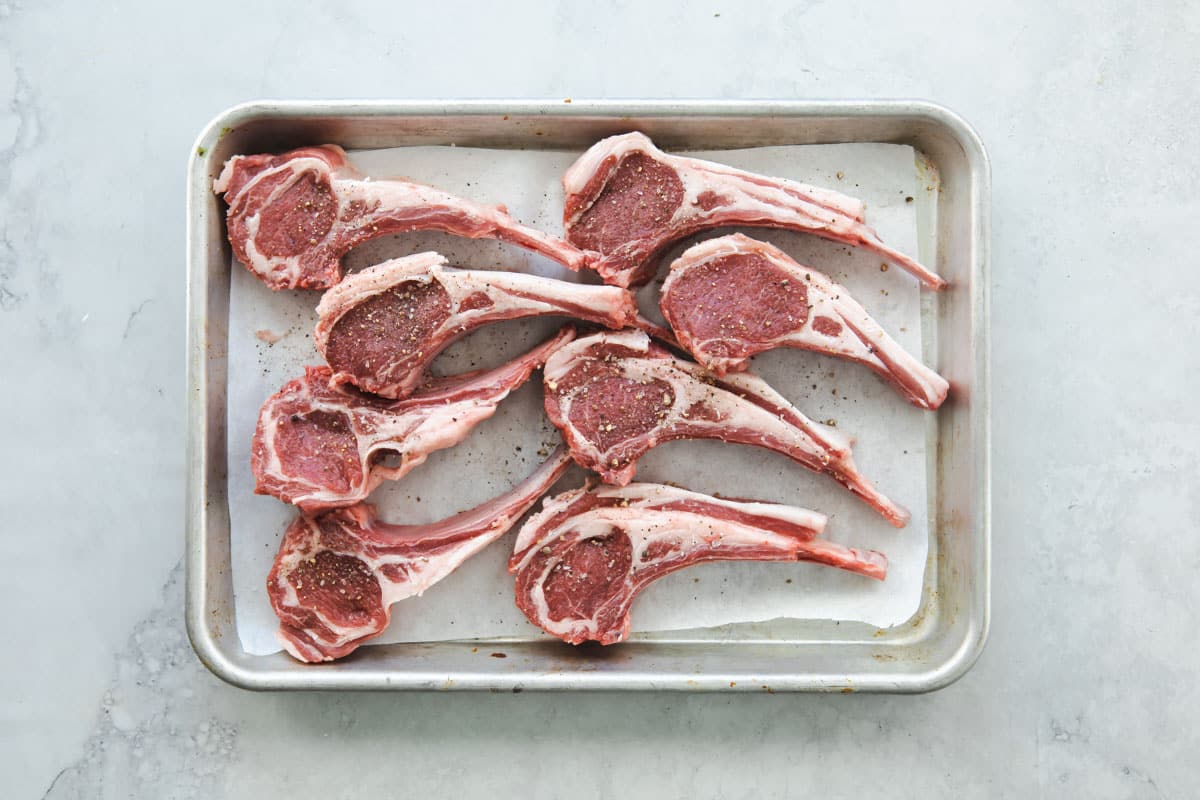 A sheet pan with 8 raw lamb chops on it.