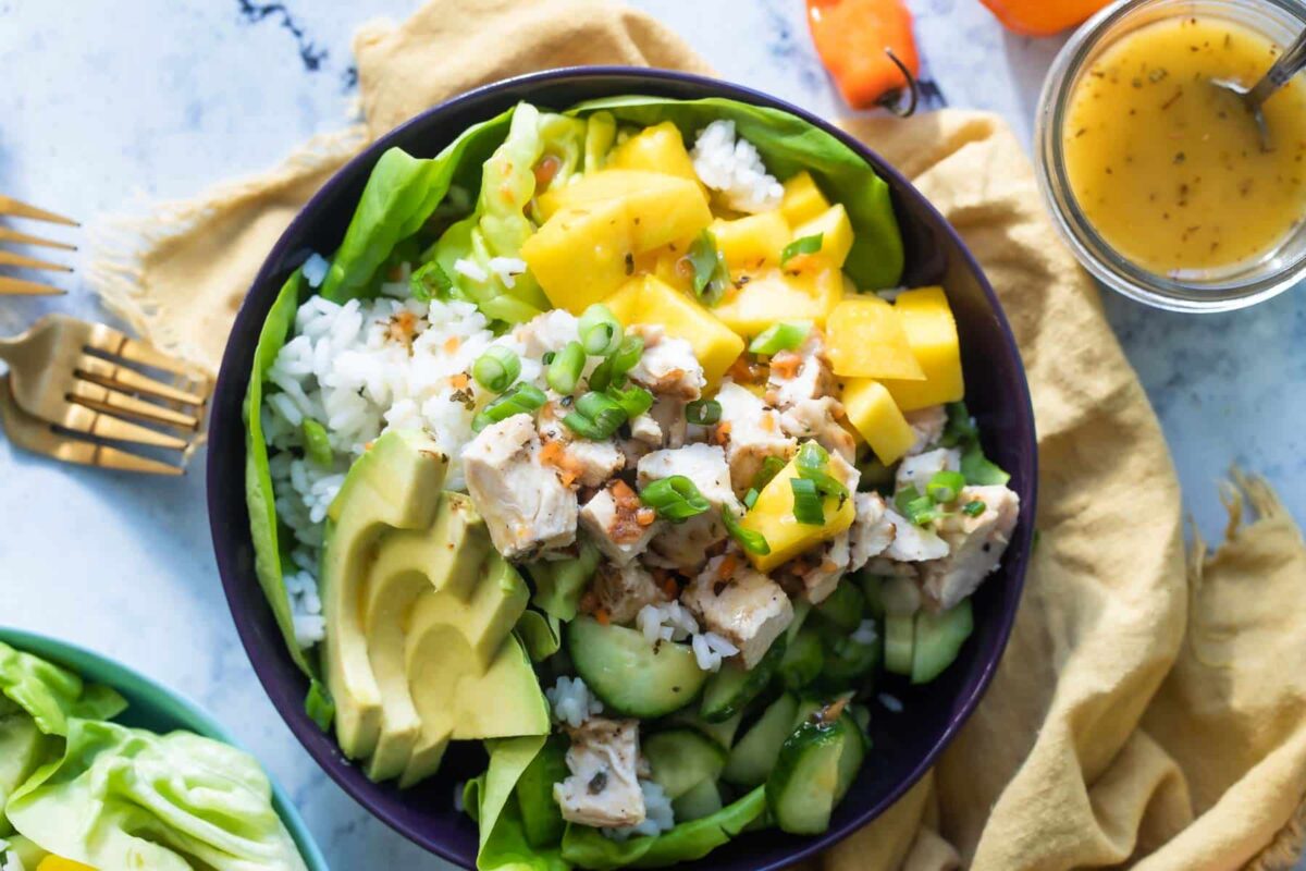 A mango chicken bowl with avocado and scallions on top.