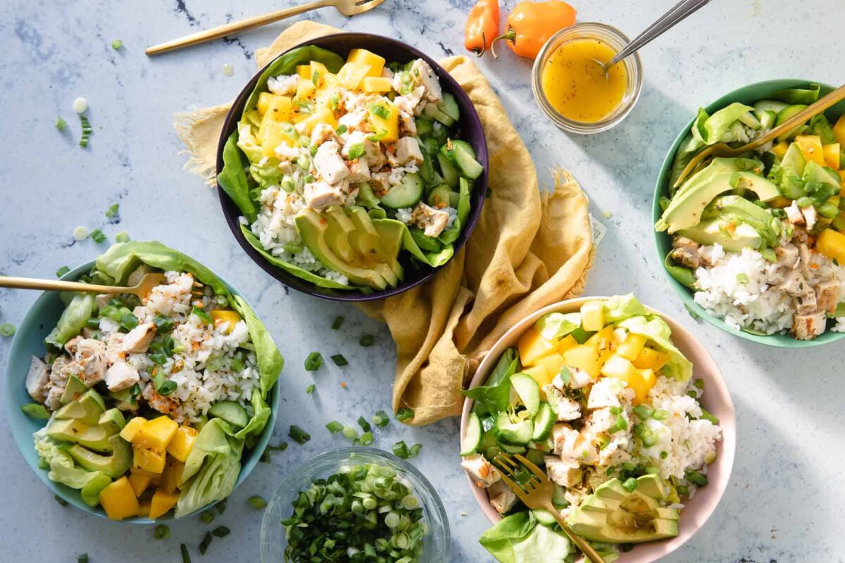 A mango chicken bowl with avocado and scallions on top.