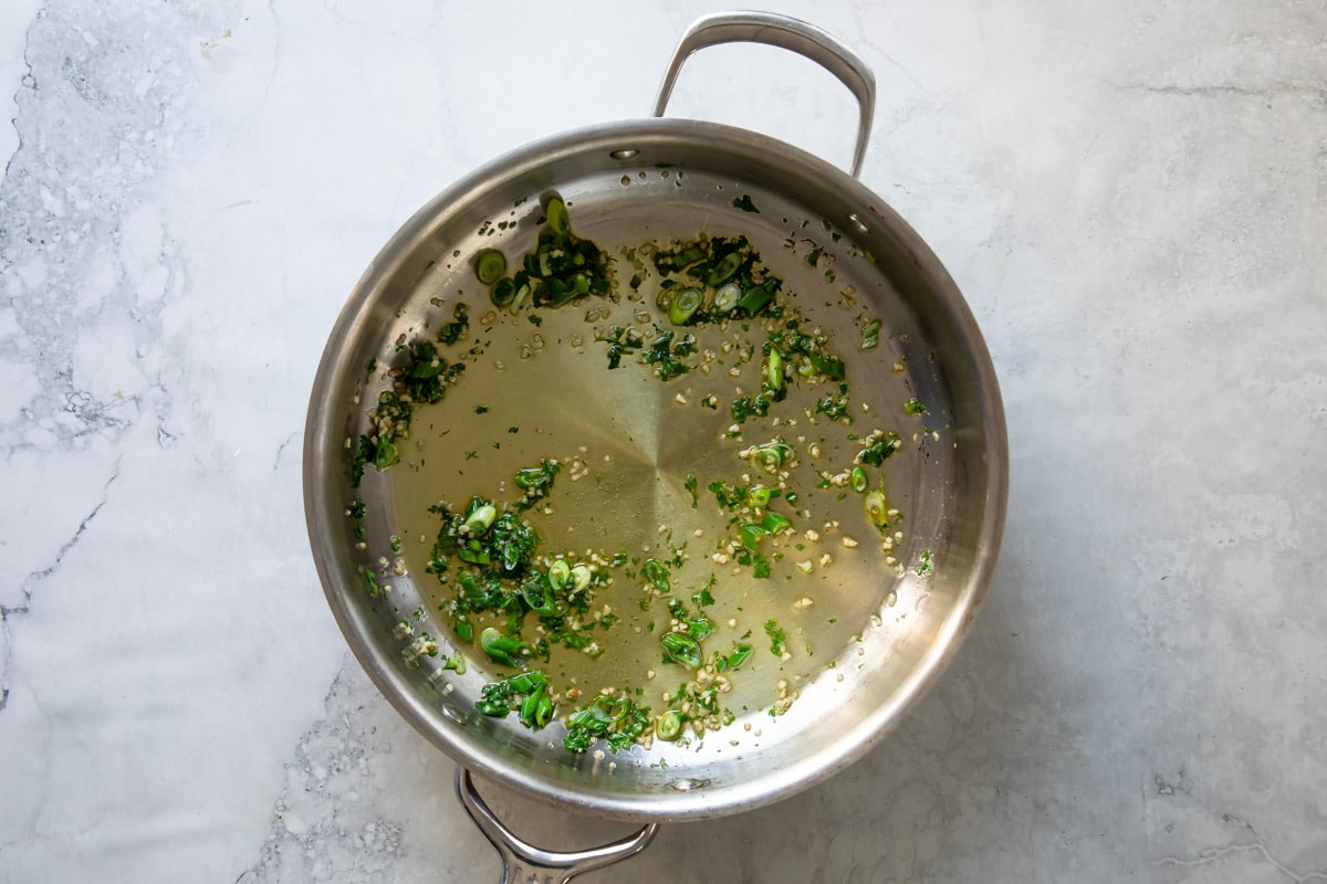 Fresh herbs cooking in a skillet in oil.