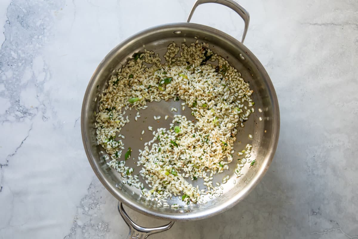 Risotto and herbs cooking in a skillet with oil.