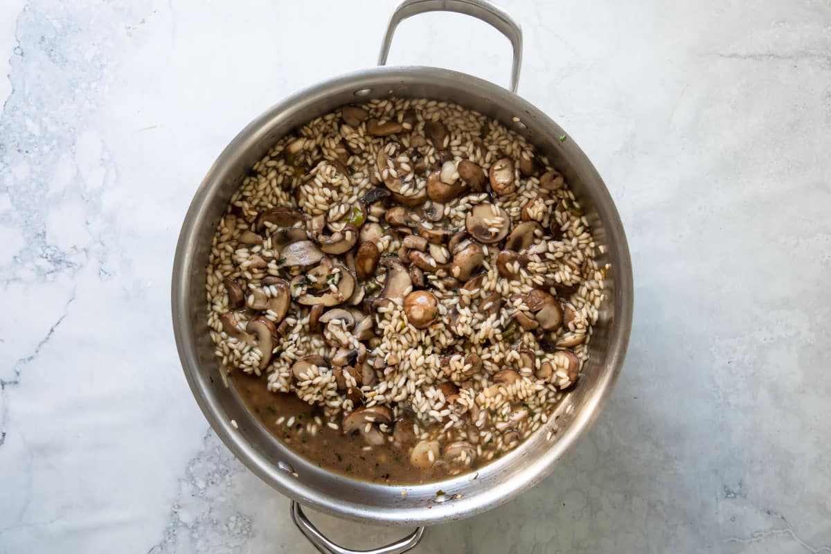 Cooking mushrooms with risotto and herbs in a skillet.