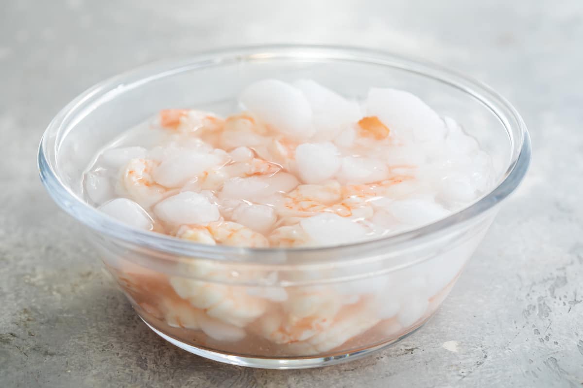 Cooked shrimp in a clear bowl of ice water.