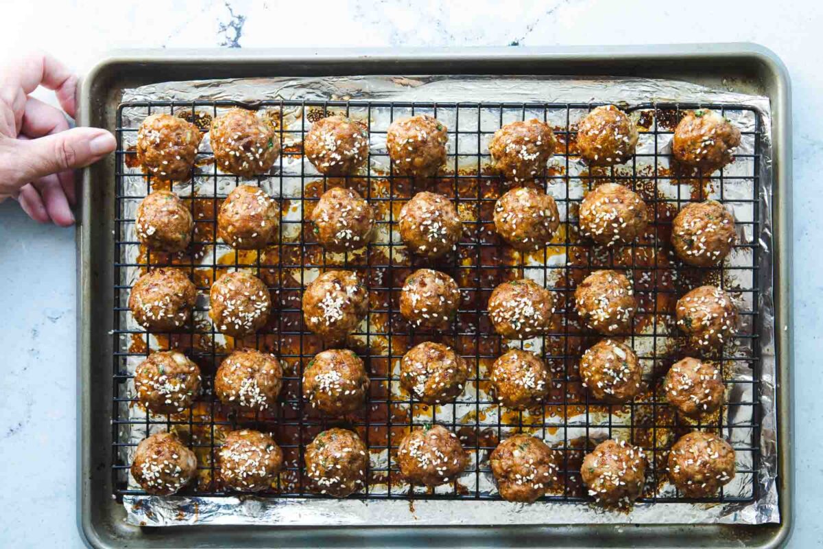 A baking rack filled with glazed teriyaki meatballs.