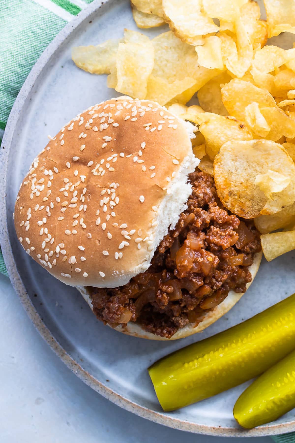 A sloppy joe on a bun with chips and pickles on a blue plate.