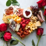 A fully-built Valentine's Day charcuterie board with roses around it.