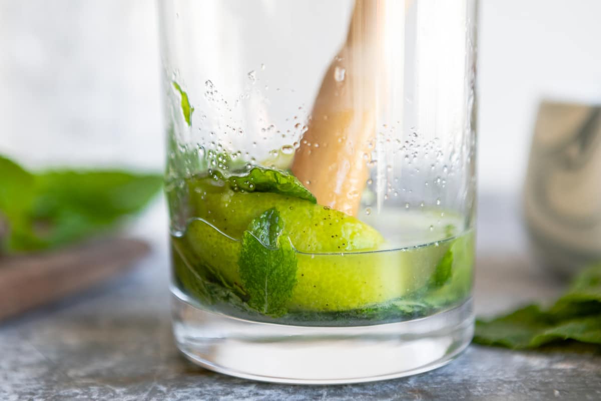 Muddling lime juice, mint, and sugar in the bottom of a glass.