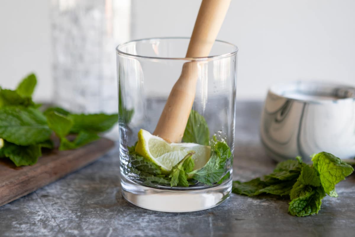 Muddling lime juice, mint, and sugar in the bottom of a glass.