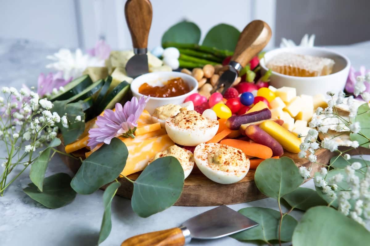 An Easter charcuterie board filled with cheese, spreads, veggies, fruit, and flowers.
