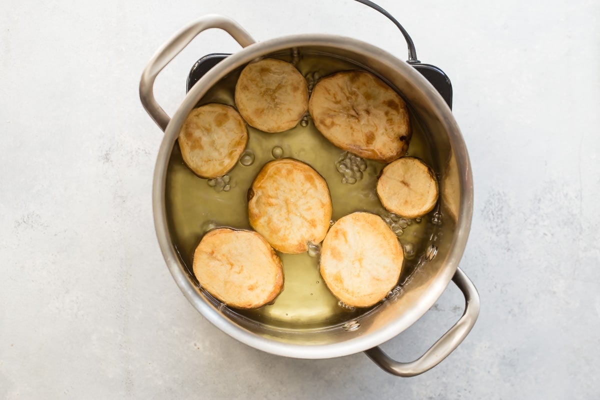 Fried potato slices frying in a pot of oil.