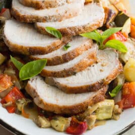 An overhead shot of pork loin with ratatouille on a white platter.