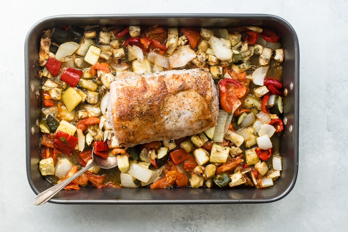 Pork loin with ratatouille in a black baking pan.