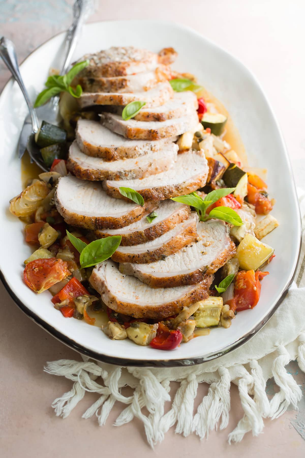 An overhead shot of pork loin with ratatouille on a white platter.