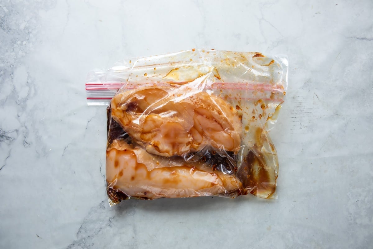 Marinading chicken breast in teriyaki sauce in a plastic bag.