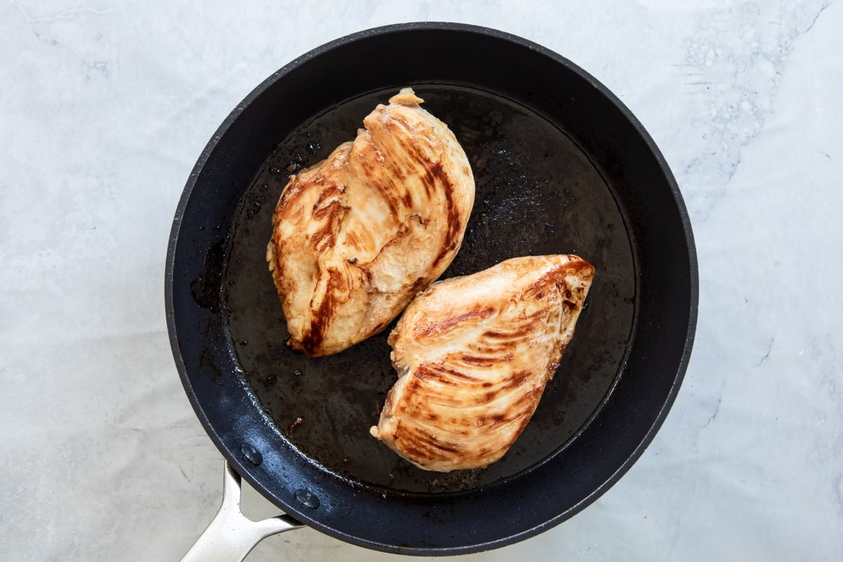 A skillet with 2 chicken breasts and teriyaki sauce.