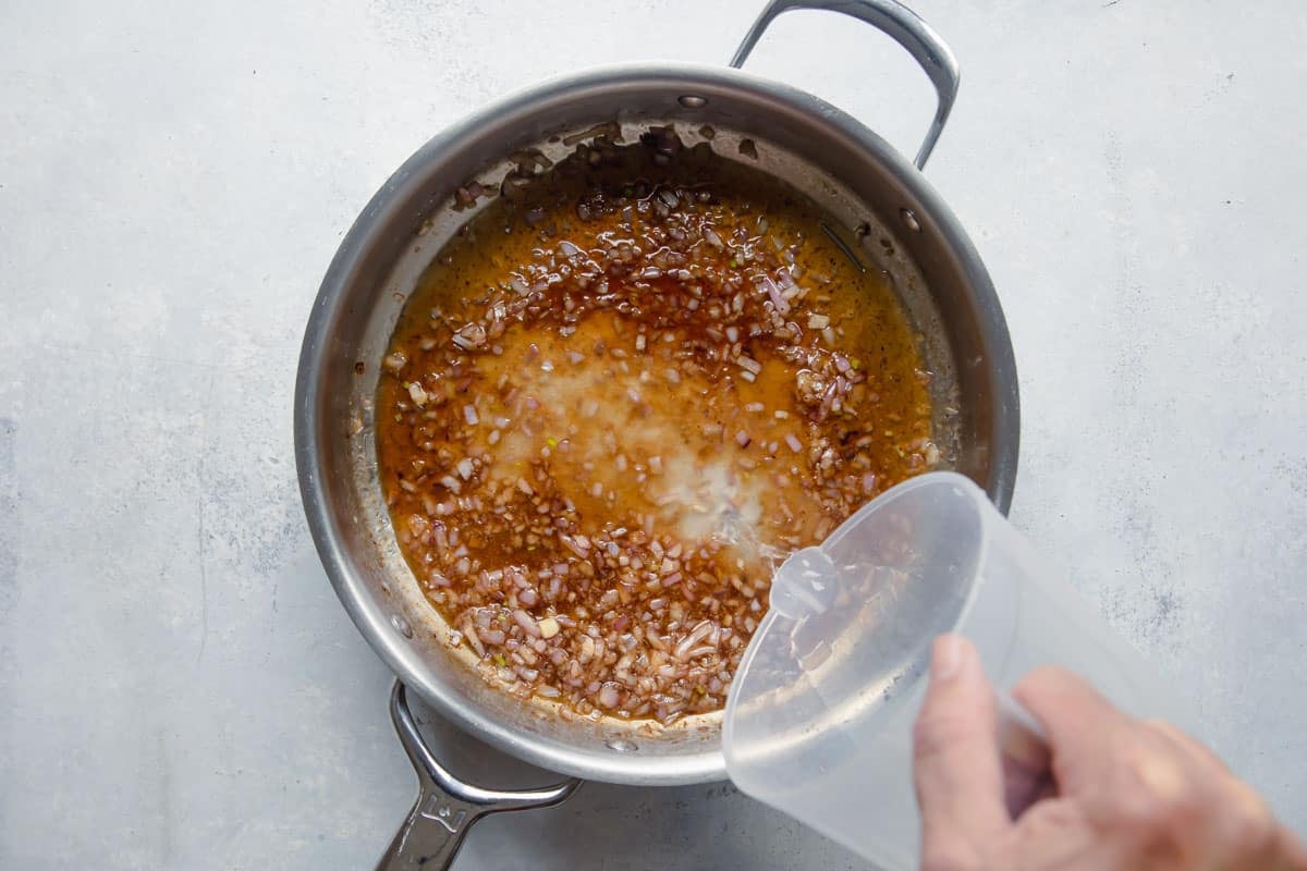 Adding vinegar to a skillet of bacon fat.