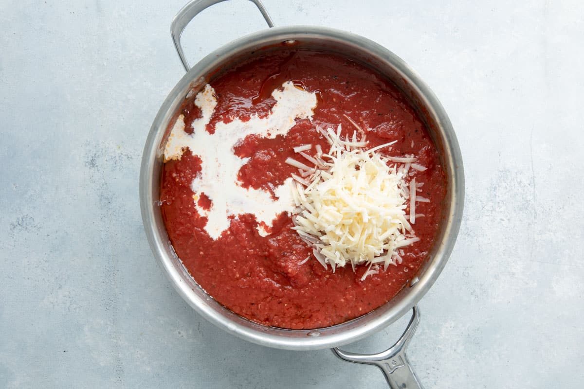 Adding heavy cream and parmesan cheese to marinara sauce in a skillet.