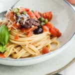 A bowl of Spaghetti alla Puttanesca on a table next to garlic bread.