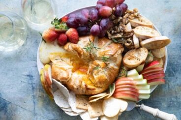 A platter with fruits, crackers and nuts with baked brie in puff pastry in the middle.
